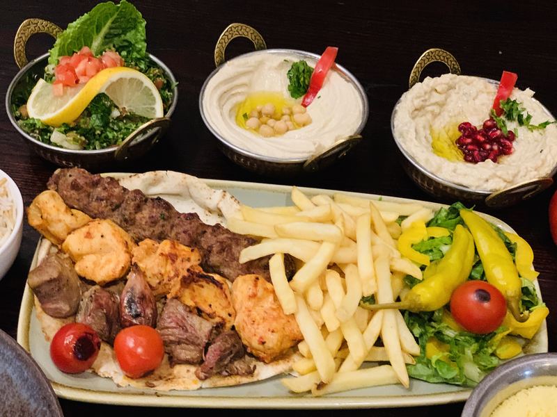 Mixed grill, chips and a spread of Lebanese mezze on a dark wooden table