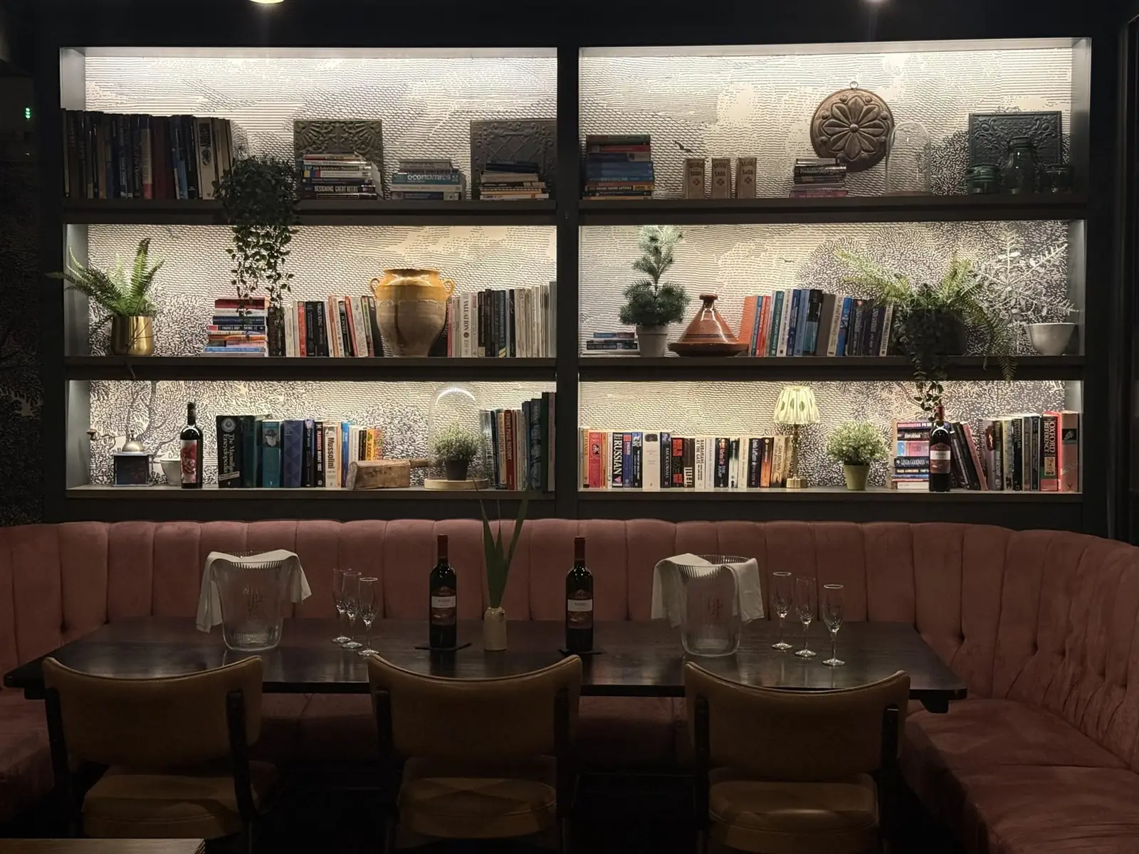 The dining room at The Reach Riverside, a family-run Mediterranean restaurant in Fulham Reach, with pink banquettes beneath a wall of books